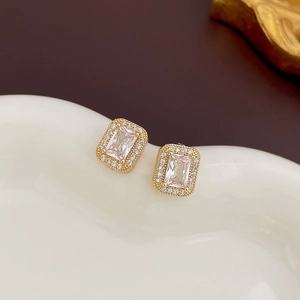 Close-up of golden square zircon stud earrings with crystal halo on white ceramic plate