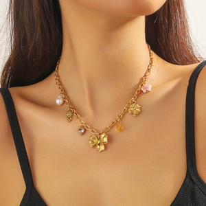 Gold-plated necklace with pink flower, bow and pearl pendants worn on a model's collarbone