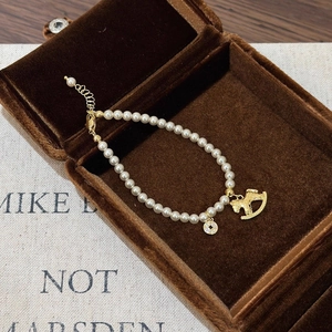 Détail d'un bracelet en perles avec breloques cheval dorées dans un écrin en velours
