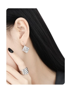 Detail showing the hammered texture on silver geometric earrings and a layered ring