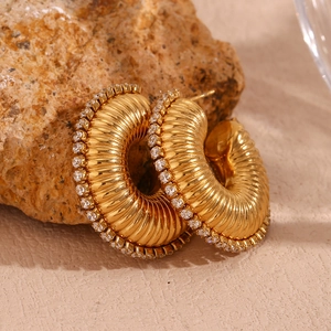 Macro view of gold plated ribbed hoop earrings with cubic zirconia on a stone background