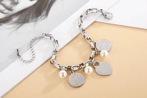 Détail d'un bracelet chaîne argenté avec pendentif cœur, perles et pièces sur fond beige