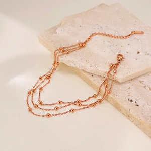 Macro detail of multi-layer rose gold stainless steel anklet with beads on stone