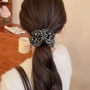 Detailed close-up of leopard print fabric scrunchie with a small gold metal logo tag