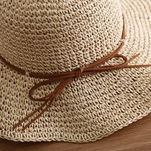 Straw sun hat for women with wide brim and brown bow detail on wooden background