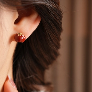 Close-up of red persimmon earrings with golden leaf details on female ear model