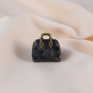 Close-up of a mini obsidian stone handbag pendant with golden handle on beige fabric