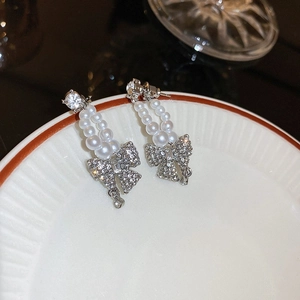 Macro detail of silver drop earrings with pearls and crystal bow pendants on a tray