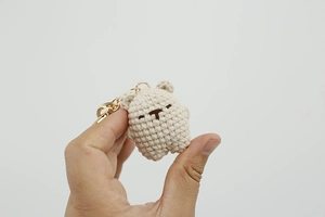 Close-up of handmade cream-colored crochet bear charm with gold metal keyring