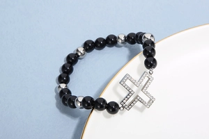 Close-up of black beaded bracelet with a large rhinestone cross on a white ceramic plate