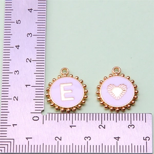 Detail view of pink enamel letter E and heart charm with ruler for size reference