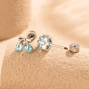 Silver cherry earrings with blue zircons and bow details on a warm sand background
