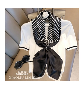 Detail of striped black and white silk scarf draped on a white knit top with luxury props