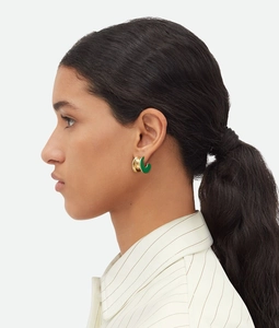 Detailed close-up of a model wearing C-shaped gold earrings with green enamel coating