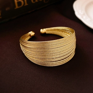 Detailed close-up of golden multi-layer wave cuff bracelet on brown velvet background