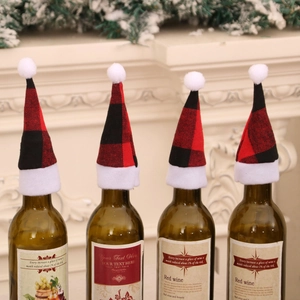 Mini red and black buffalo plaid wine bottle covers with white pom-poms on a fireplace