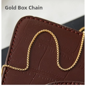 Macro shot of polished gold box chain on dark leather texture with close-up details