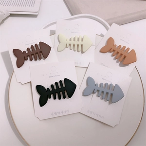 Flat lay detail of five candy-colored fishbone hair clips in matte finish on white tray