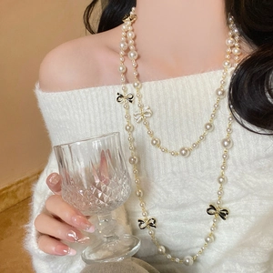 Detail of layered pearl necklace with black bow pendant on elegant white sweater