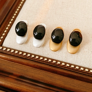Detail of silver and gold metal earrings with black oval resin stones on linen