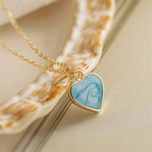 Macro shot of light blue marble heart pendant on fine golden necklace over shell