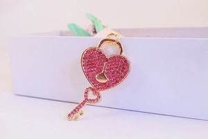 Detailed view of a gold heart lock and key keychain with pink rhinestones on a white box