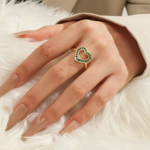 Detailed view of an open heart ring with green stones on a gold-plated band