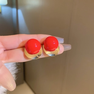 Dettaglio degli orecchini a lobo a sfera rossa con base in metallo dorato lucido