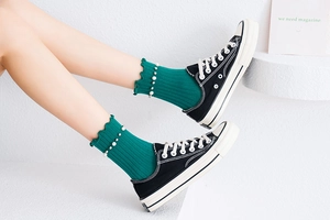 Detail of green knit socks featuring ruffled edges and delicate pearl embellishments