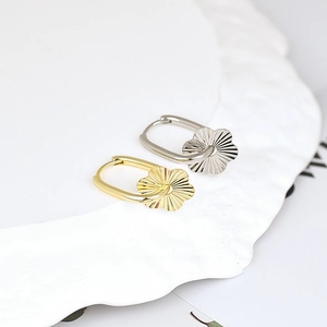 Elegant gold and silver flower pendant earrings on a white tray, minimalist retro style