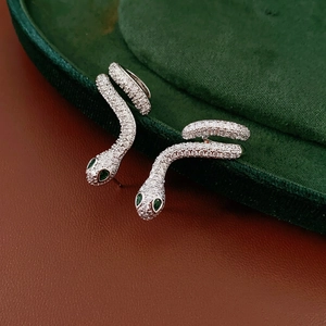 Silver snake earrings with white crystals and green gemstone eyes in a retro luxury style