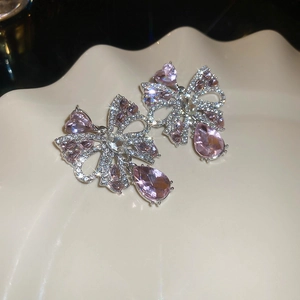 Macro detail of silver bow drop earrings with pink crystal pendants on a cream plate