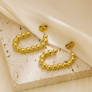Detail of gold-plated beaded C-shape earrings on stone base with champagne silk fabric
