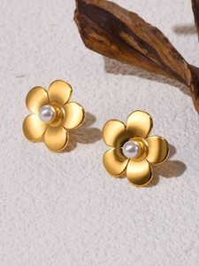 Macro shot of gold floral earrings with a white pearl center on a white stone background