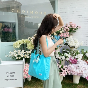 Detalle de bolso tote de lona azul con asa de cuadros y etiqueta blanca decorativa