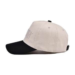 Side view of beige and black baseball cap with embroidered lettering and curved brim