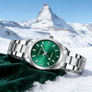 Detail of silver steel watch with green dial and diamond markers against snow mountain background