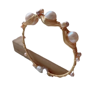 Handmade gold wire wrap bangle with elegant pink freshwater pearls on a wooden stand