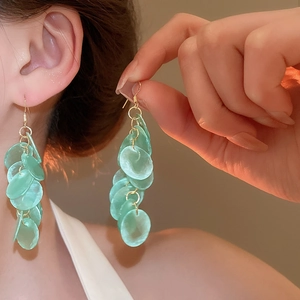 Detail of long fringe earrings with light green translucent scales and gold-tone hooks