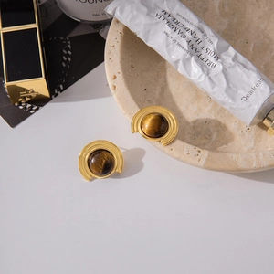 Detail of 18K gold-plated ribbed earrings with round tiger eye stones on marble tray