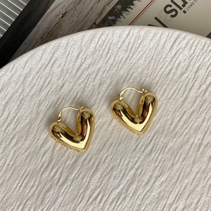 Primer plano de pendientes de aro con forma de corazón dorado en plato cerámico
