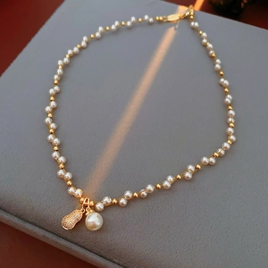 Macro detail of gold-plated necklace with white pearls and a gourd-shaped zircon pendant