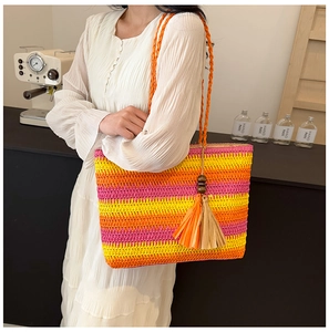 Detail of handmade straw tote bag with vibrant yellow, orange and pink stripes and tassels