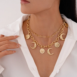 Detail of double-layer gold necklace with moon and sun pendants on a white shirt