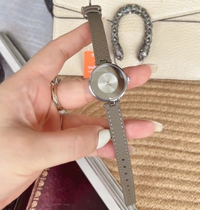 Detailed close-up of a silver watch dial with taupe leather strap held by hand
