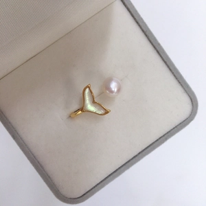 Dettaglio macro di un anello a coda di pesce dorato con perla e conchiglia in scatola