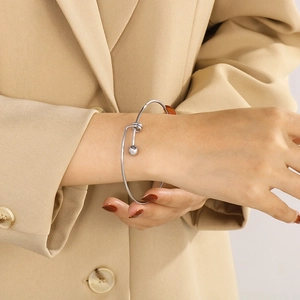 Close-up of a minimalist silver steel ball cuff bracelet worn over a beige sleeve