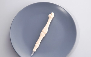 Detailed macro view of bone-shaped ballpoint pen in off-white resin on a blue tray