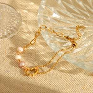 Golden stainless steel heart pendant bracelet with pearls on a vintage glass tray