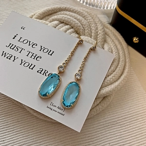 Elegant gold earrings with blue oval crystals and zircon tassels on a white gift card